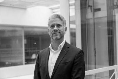 A confident man in a suit standing indoors with a slight smile.