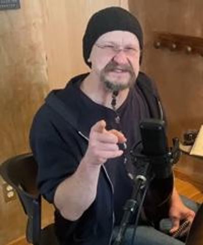 Joe sitting in a chair smiling, pointing at you.