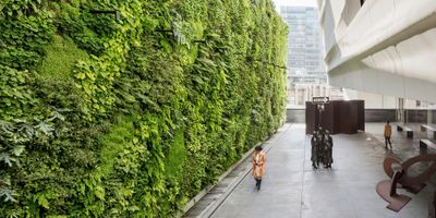 A large vertical garden wall in an urban outdoor space with sculptures and a child walking.