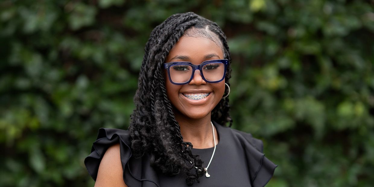 Smiling young woman with glasses and braided hair outdoors.