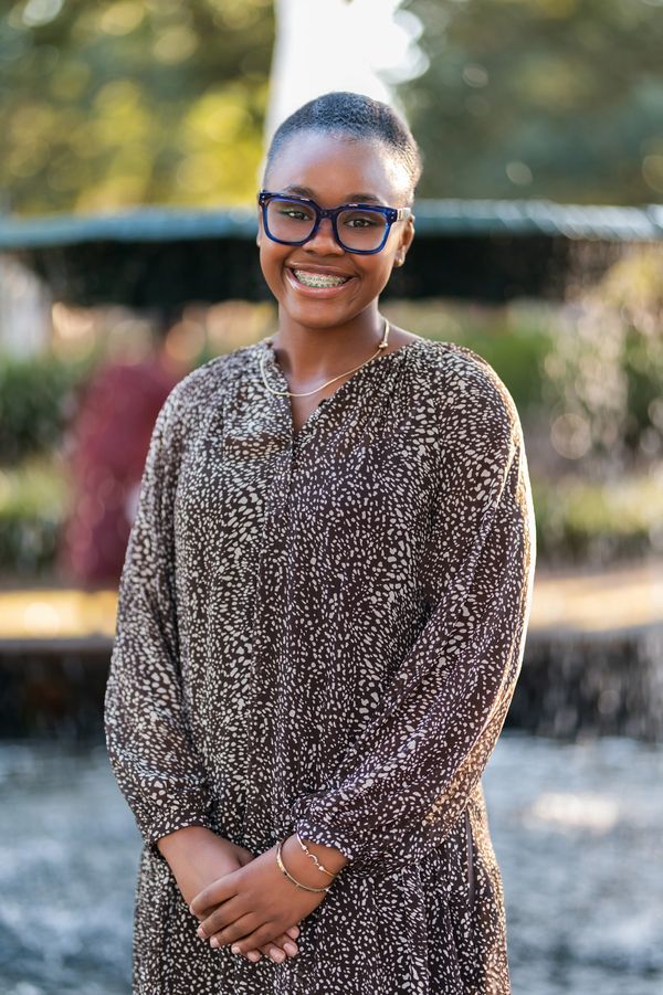 Young woman smiling confidently with glasses and braces outdoors.