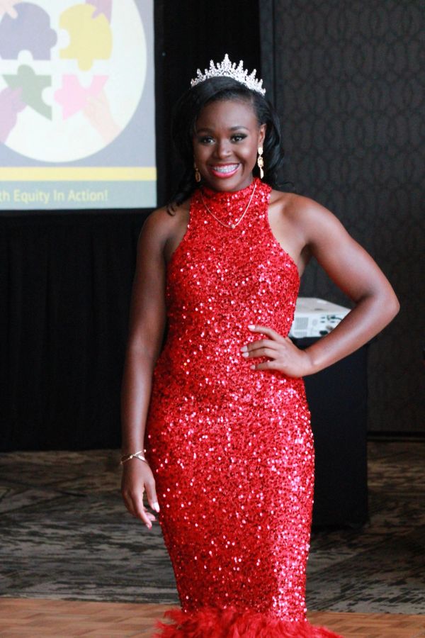 Young woman in a sparkling red gown and tiara smiles confidently.