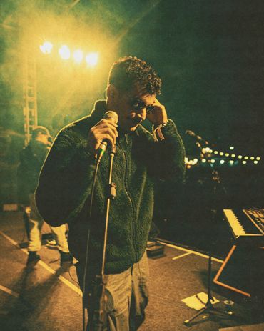 A performer adjusting his glasses on stage with warm lighting.