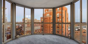 Empty room with large windows overlooking city buildings.