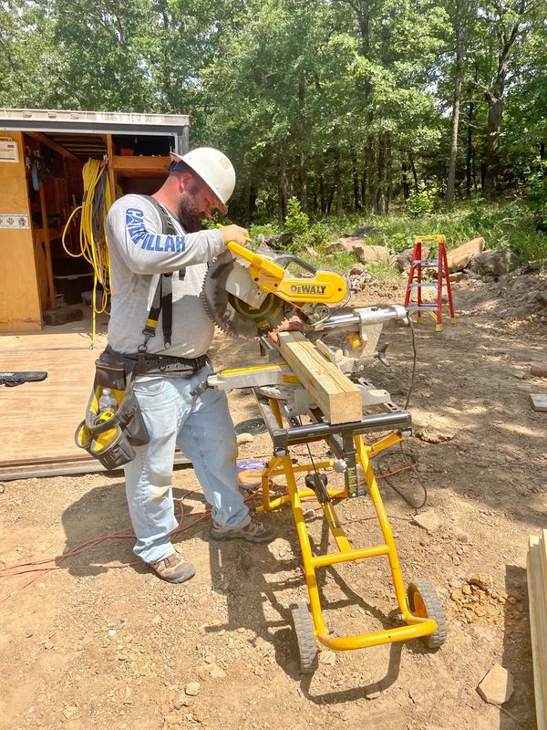 Carpenter wearing tool belt and hard hat making a cut in a 4x4 post using a DeWalt saw 