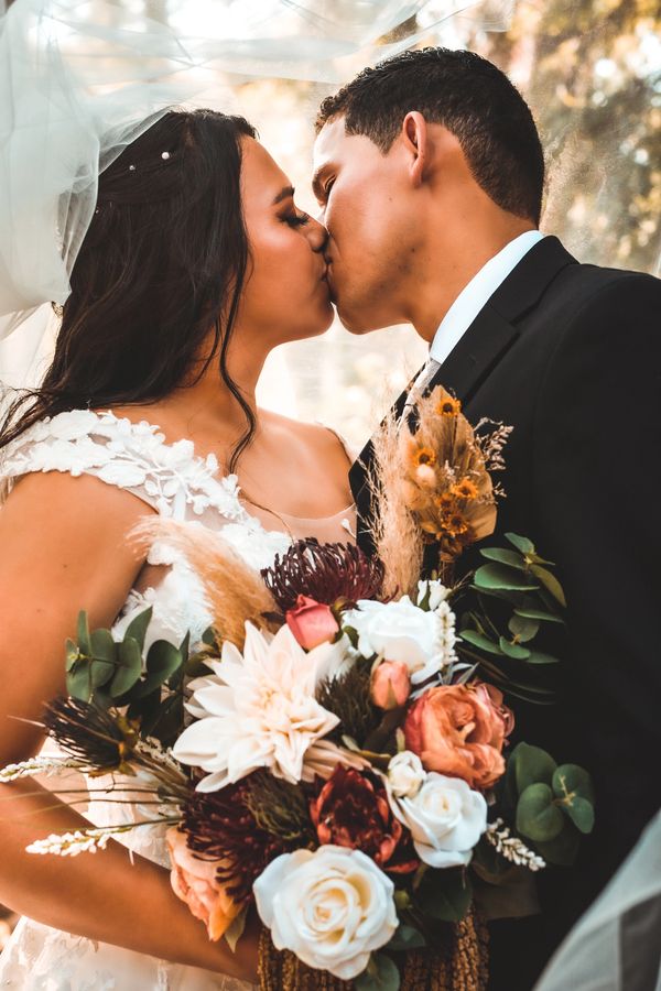 Bride and groom sharing a kiss on their wedding day, holding a beautiful bouquet.