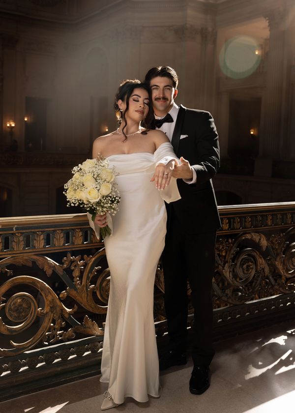 A bride and groom posing elegantly in formal wedding attire indoors.