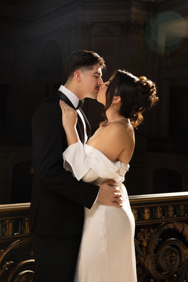 A couple in formal attire sharing a tender kiss indoors.