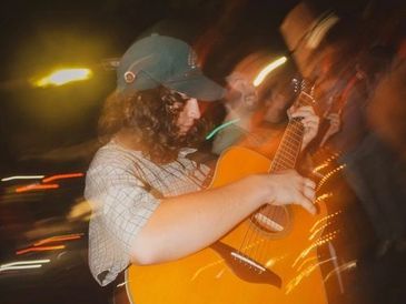Person playing guitar in a dimly lit, blurry setting.