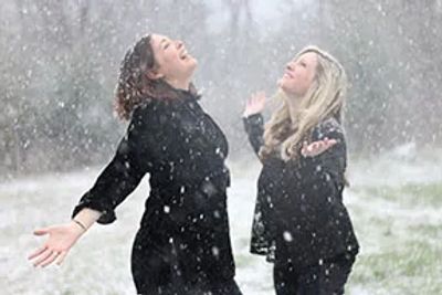 Two women joyfully enjoying a snowy day outdoors.