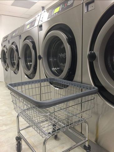 Row of industrial washing machines with a laundry cart in front.