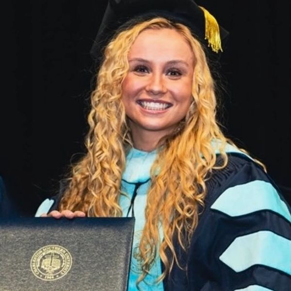 Smiling graduate in cap and gown holding diploma.