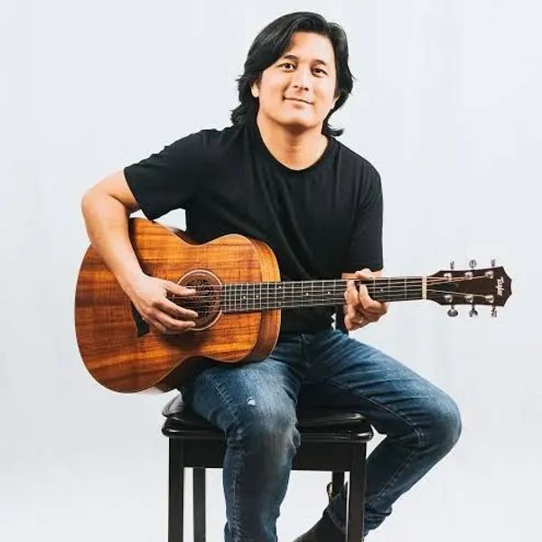 Man sitting and playing an acoustic guitar with a smile.