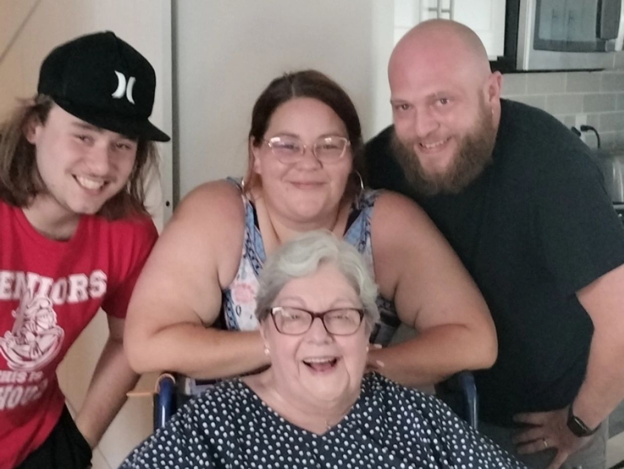Four generations of family smiling together in a cozy kitchen.