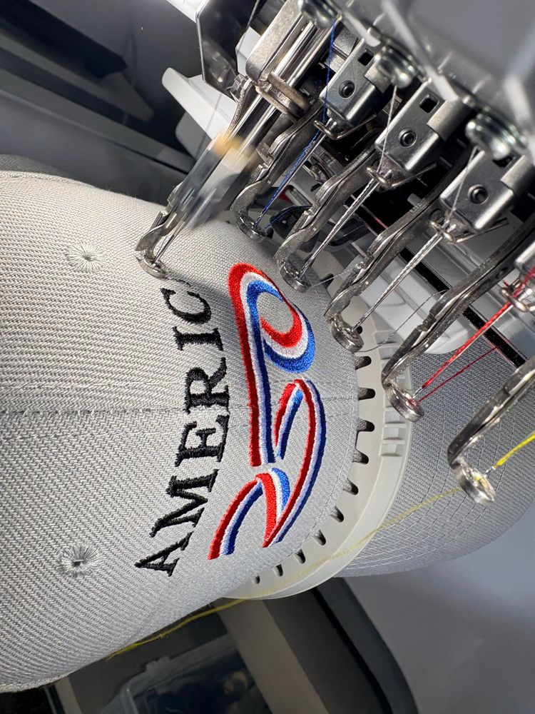 Embroidery machine stitching a colorful 'AMERICA' logo on fabric.