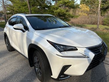 White Lexus NX parked on a road with trees in the background.