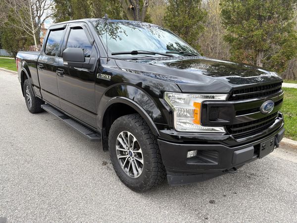Black Ford F-150 truck parked on a street with trees in the background.
