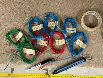 Coiled colored wires with tools and measuring tape on carpet.