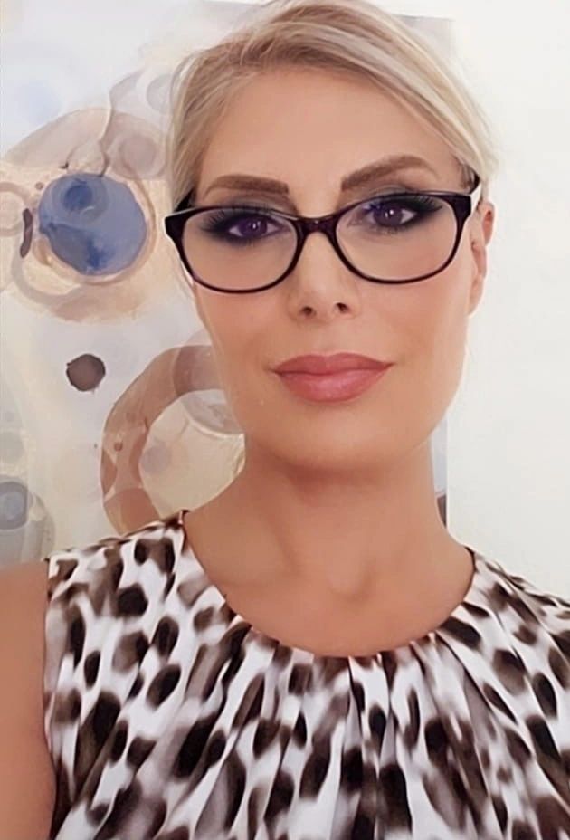 Woman with glasses and animal print top smiling at the camera.