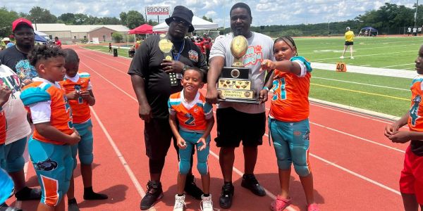 Youth football team with coaches holding championship trophies on a track.