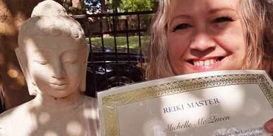 Woman smiling with Reiki Master certificate and Buddha statue.