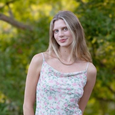 Young woman in a floral dress posing outdoors with a gentle smile.