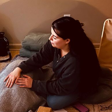 A woman sitting on cushions, looking to the side thoughtfully.