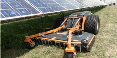 Autonomous robotic mower cutting grass near solar panels.