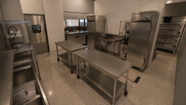 Modern, clean commercial kitchen with stainless steel tables and appliances.
