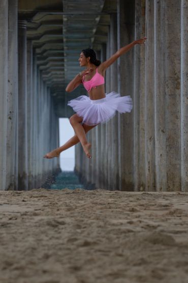 Ballerina jumping under a pier on the beach.