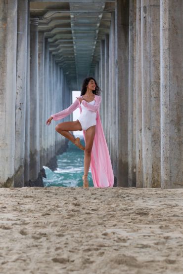 Ballerina dancing under a pier on the beach.