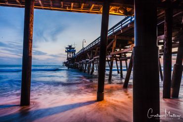 View under a wooden pier at sunset with waves.