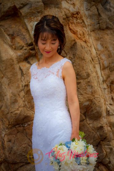 Bride in white dress holding bouquet against a rocky background.