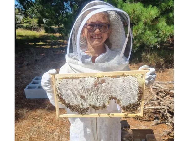 Beekeeper in beesuit inspecting frame of honey