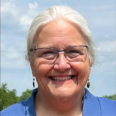 Smiling elderly woman with white hair and glasses outdoors.