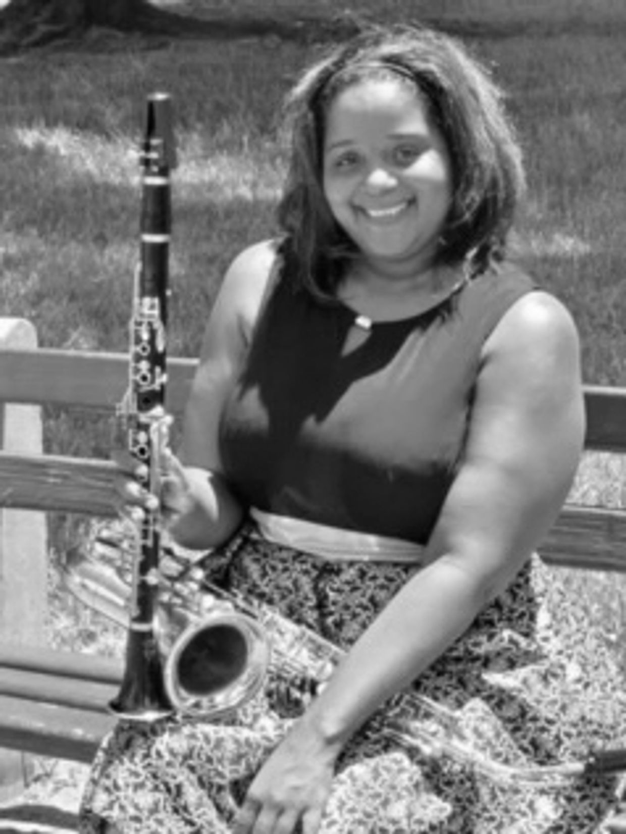 A woman sitting on a bench smiling, holding a saxophone and clarinet.