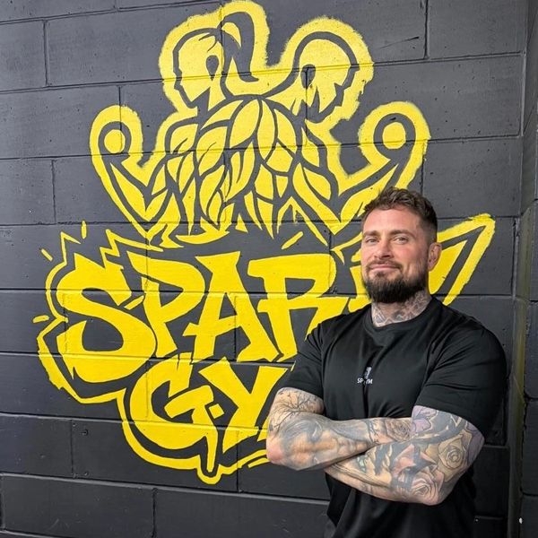 Man with tattoos standing in front of a gym mural.