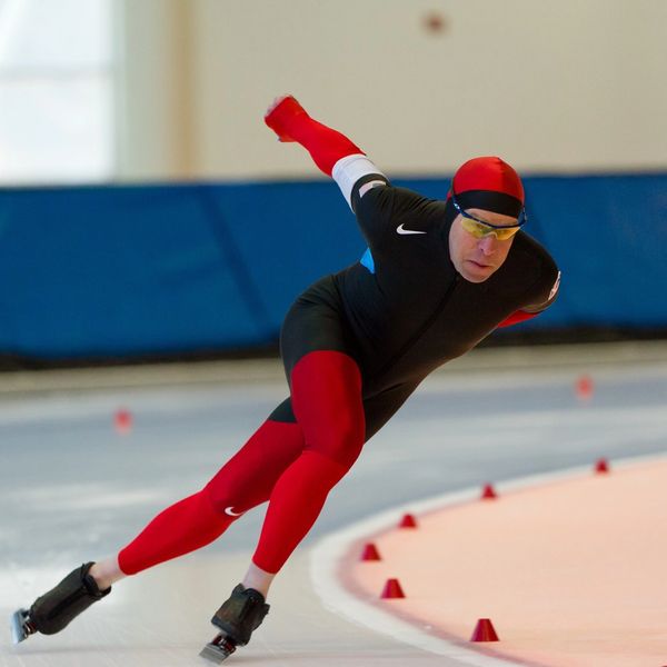 Speed skater in red and black racing on an ice track.