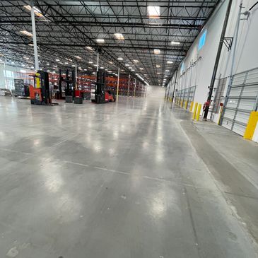 Spacious warehouse interior with forklifts and high shelves under bright lighting.