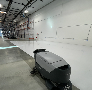 A floor cleaning machine in a large empty warehouse.