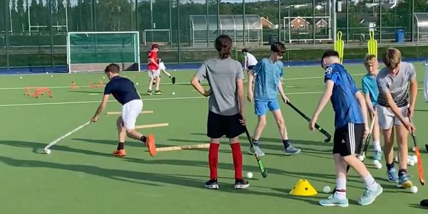 Young players practicing field hockey skills on a green turf field.