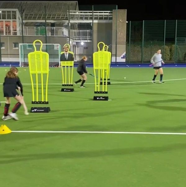 Kids practicing field hockey with training mannequins on a turf field at night.