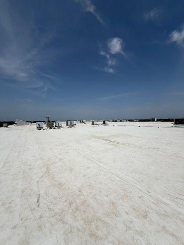 Wide view of a flat white rooftop under a blue sky with scattered clouds.