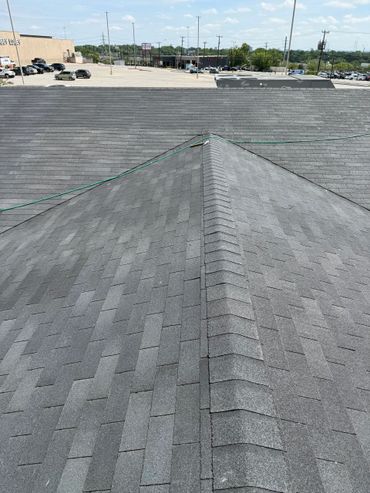 View of a gray shingled rooftop under a clear sky with a parking lot in the background.