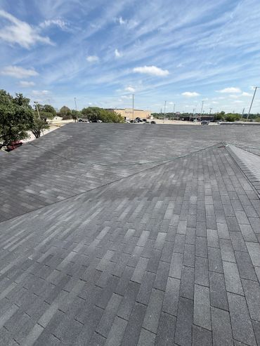A rooftop with gray shingles under a partly cloudy sky.