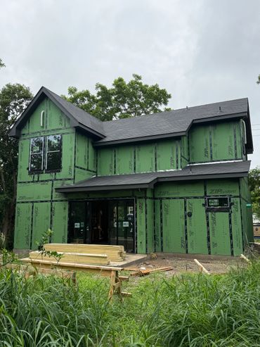 Two-story house under construction with green sheathing and black roof.