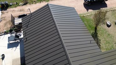 A modern dark metal roof on a house with outdoor seating.