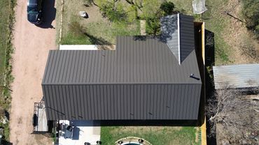 Aerial view of a house with a dark metal roof and surrounding yard.