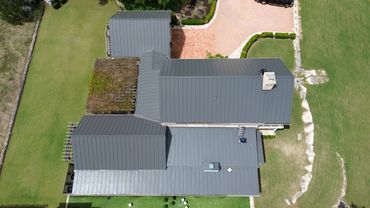 Aerial view of a house with a metal roof and a green lawn surrounding it.