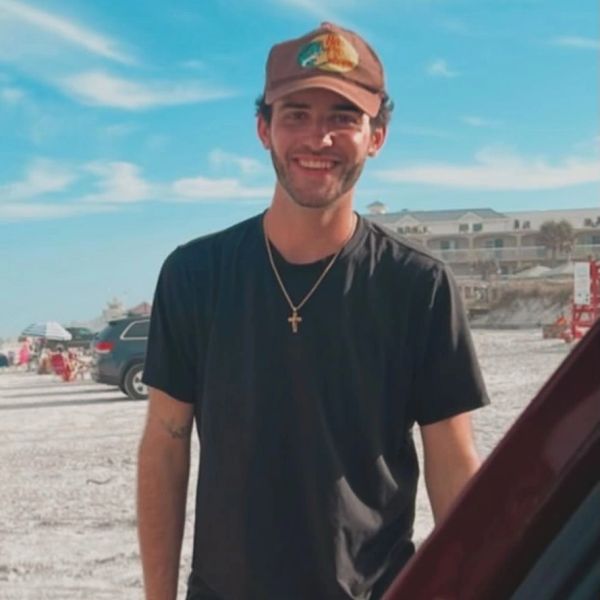 Smiling young man in a black t-shirt and cap at a sunny beach.